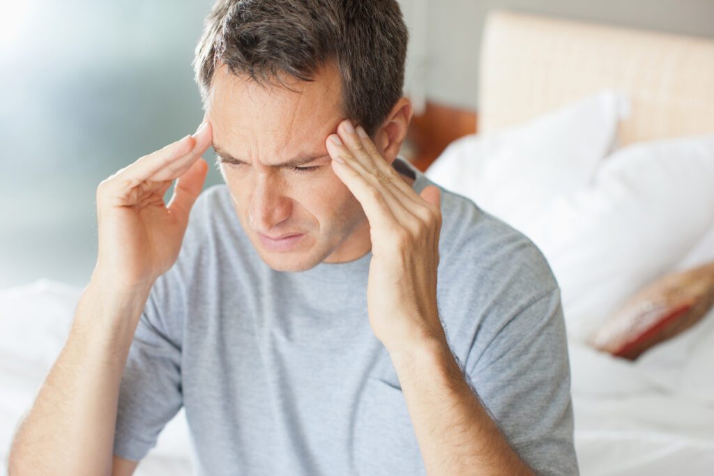 Man sitting on bed with hands on the side of his head headache credit Paul Bradbury الصداع الجنسي وطرق علاجه